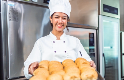 smiling food handler in chef's uniform carrying tray of rolls