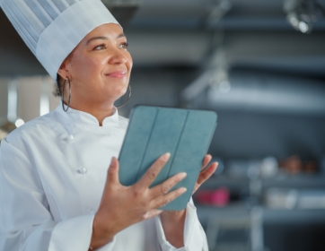 a smiling woman in a chef's hat holding a table while she works